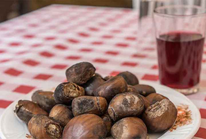 Plato de castañas asadas con la piel tostada sobre un mantel de cuadros rojos y blancos, junto a un vaso de vino tinto nuevo, la mesa típica de San Andrés en Tenerife.