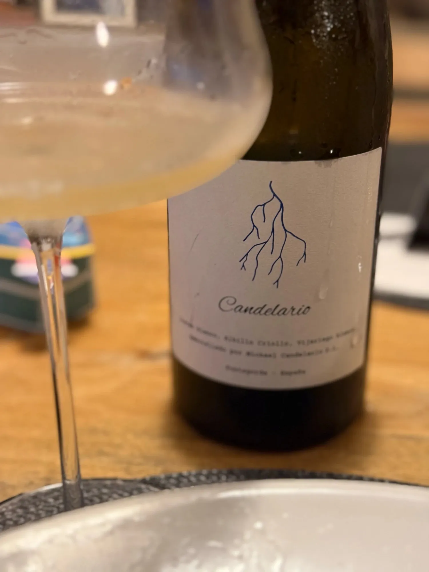 Botella del Candelario Blanco 2025 de Michael Candelario, un blanco de Puntagorda en La Palma, con su etiqueta blanca y un rayo azul dibujado a mano, junto a una copa de vino blanco pálido sobre una mesa de madera.